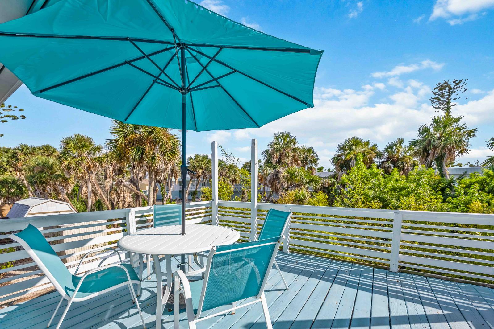 Blue Gecko private outdoor porch with table, chairs and umbrella overlooking palm trees at Gecko House Manasota Key