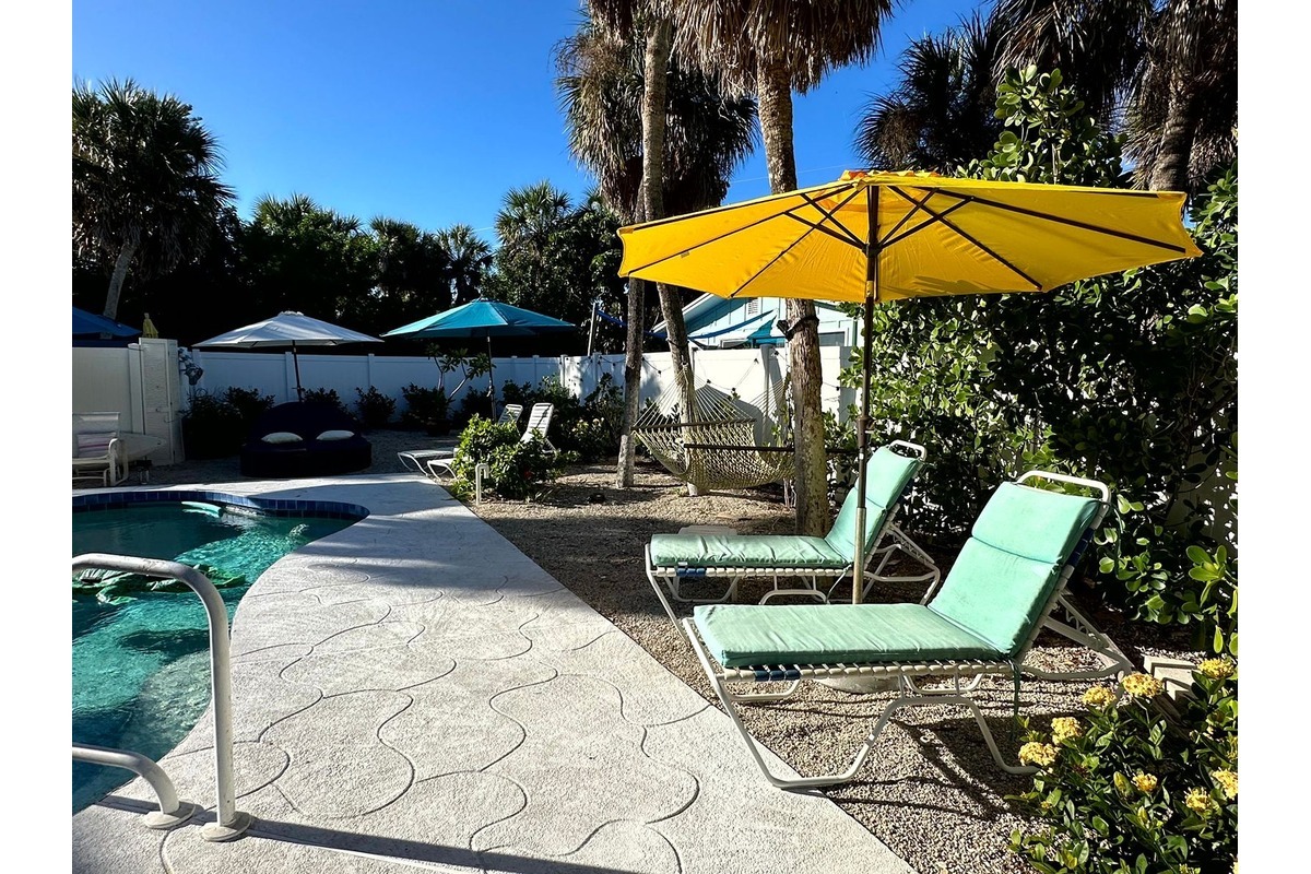 Poolside patio at Gecko House with a yellow umbrella and teal lounge chairs