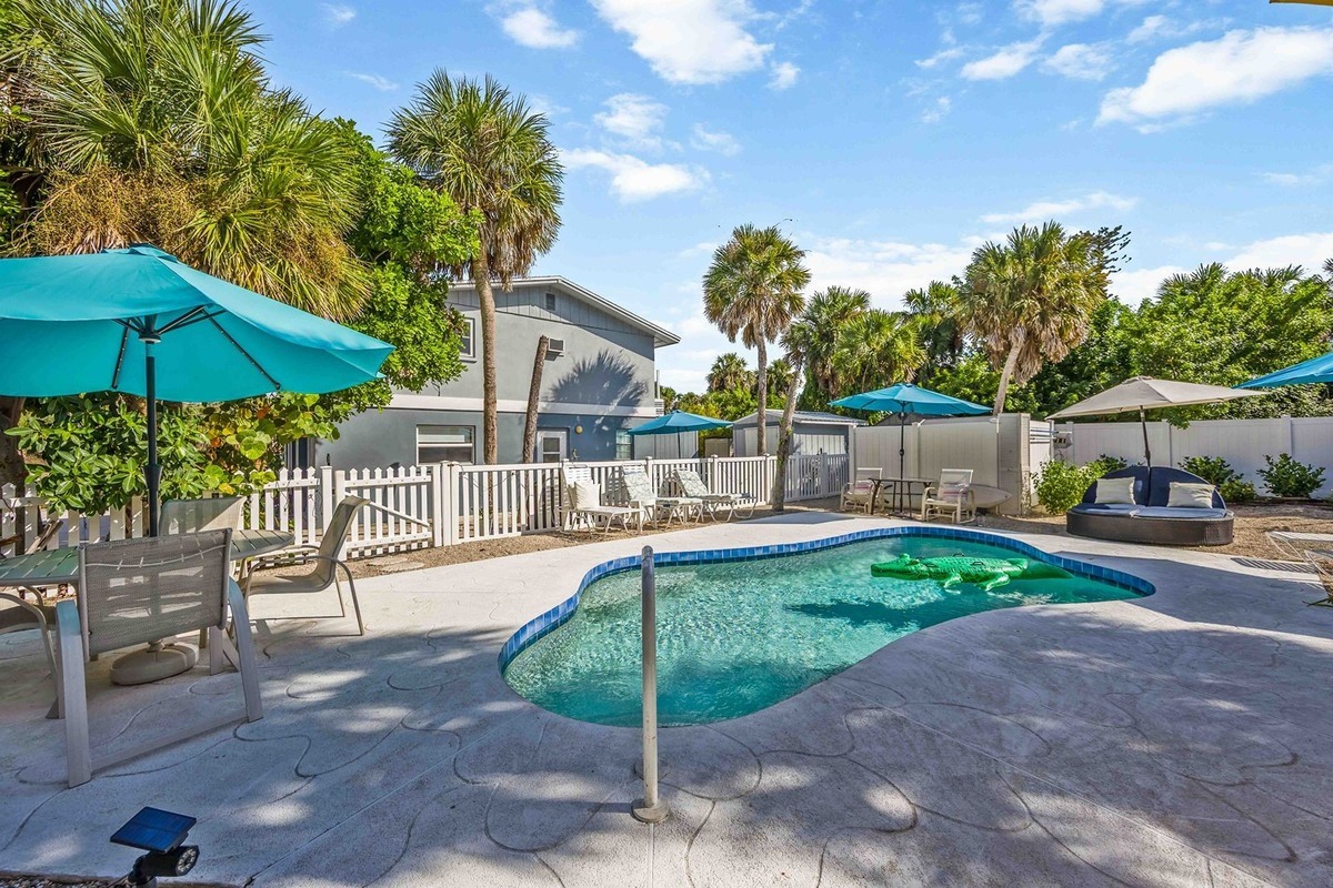 Gecko House pool on a clear day, ringed by teal umbrellas and patio seating